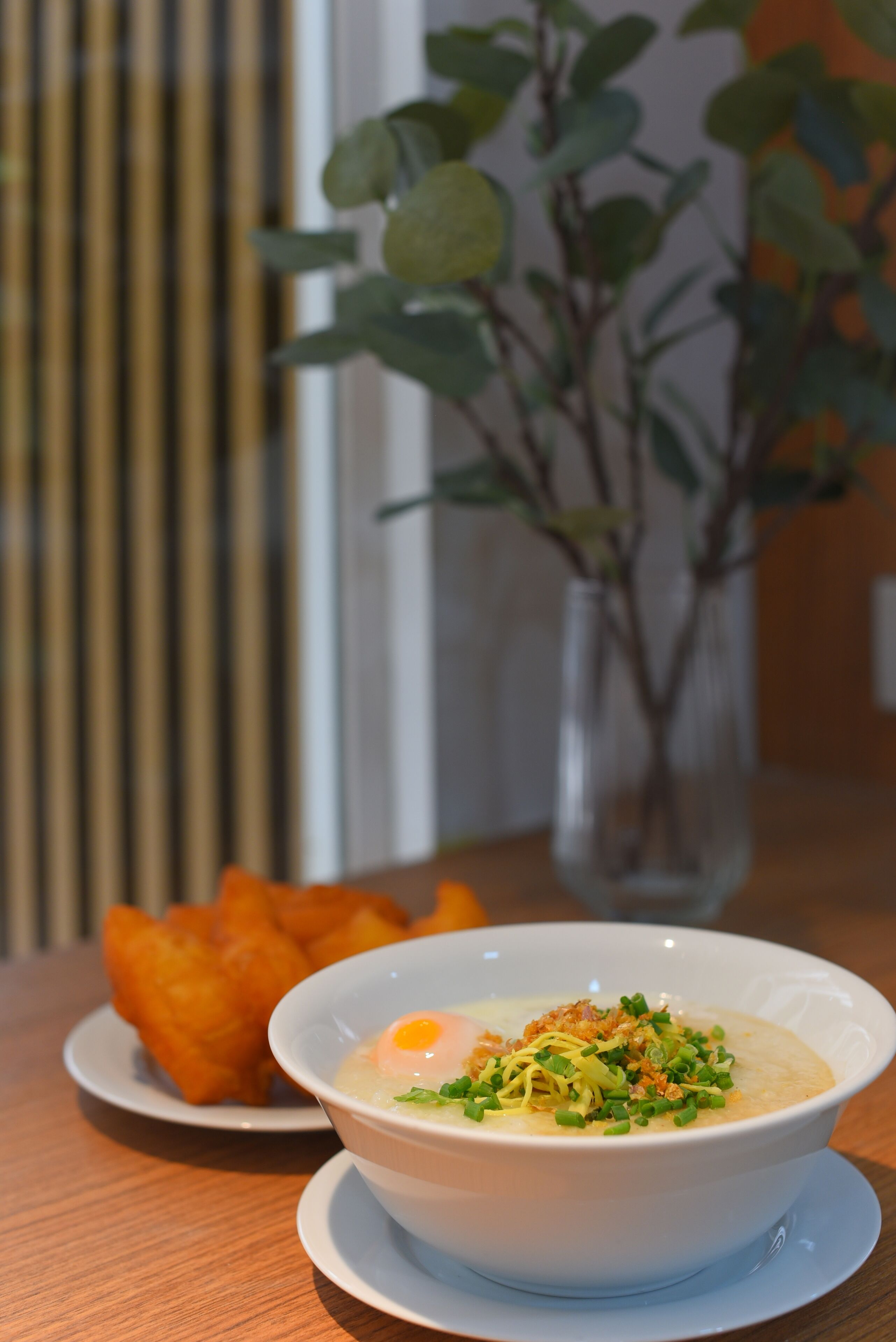 Eine Schüssel Suppe mit pochiertem Ei und grünen Garnelen, dazu frittierte Beilagen auf einem kleinen Teller.