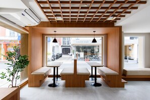 Un interior moderno con bancos y mesas de madera, ventanas amplias y un equipo de aire acondicionado.