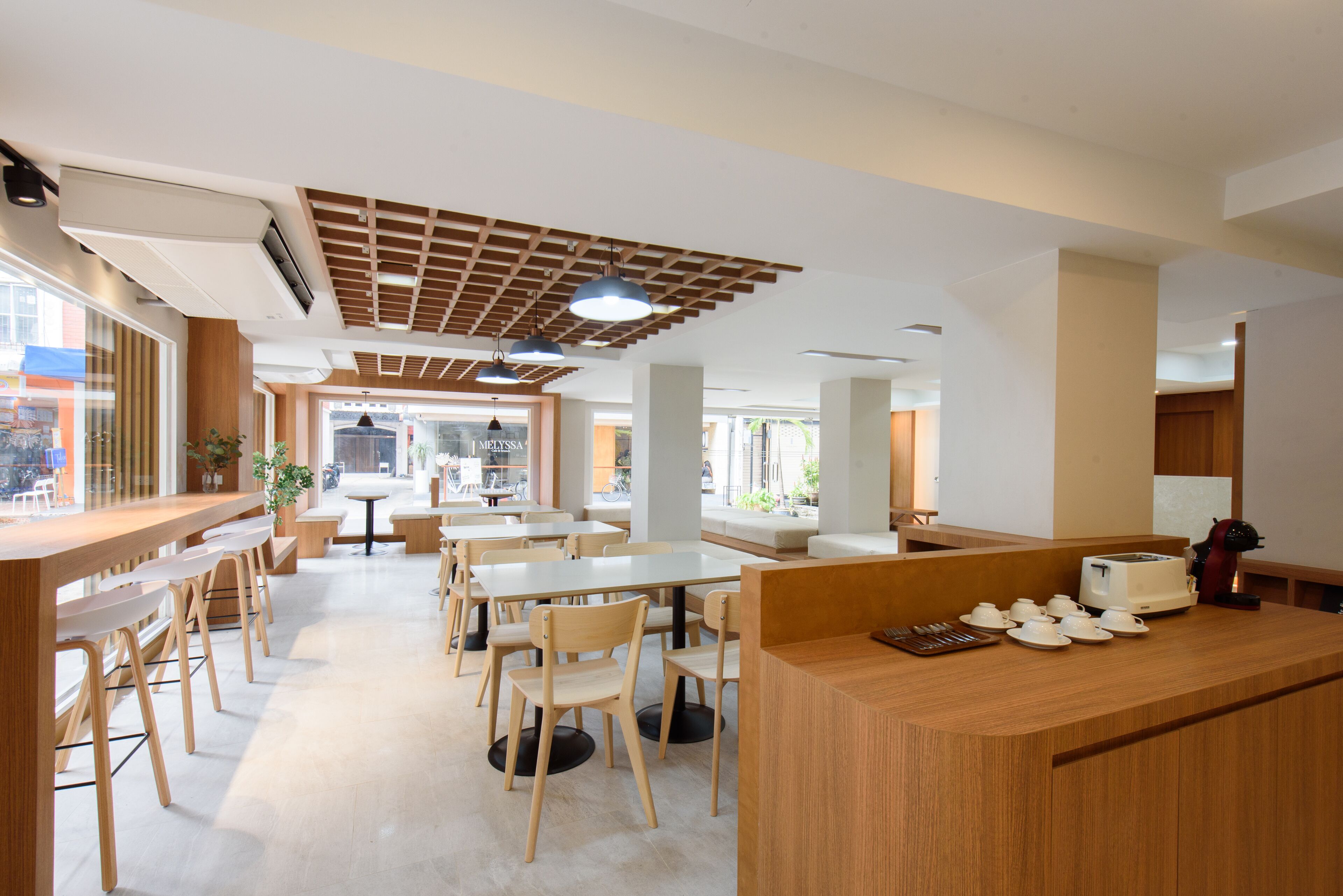 A modern restaurant with wooden furniture, a counter with tea sets, and large windows.