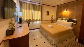 A hotel room with a bed, a desk, a chair, a TV, and a wall-mounted light. - Honey House 2 (Bangkok)