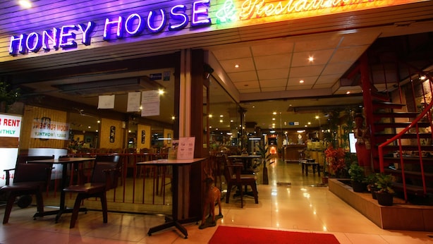 The exterior of Honey House Restaurant with a neon sign, outdoor seating area, and a staircase leading to the entrance. - Honey House 2 (Bangkok)