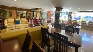 A spacious indoor area with a yellow sofa, wooden dining table, and chairs. There are bookshelves with various items and a glass partition with plants. - Honey House 2 (Bangkok)