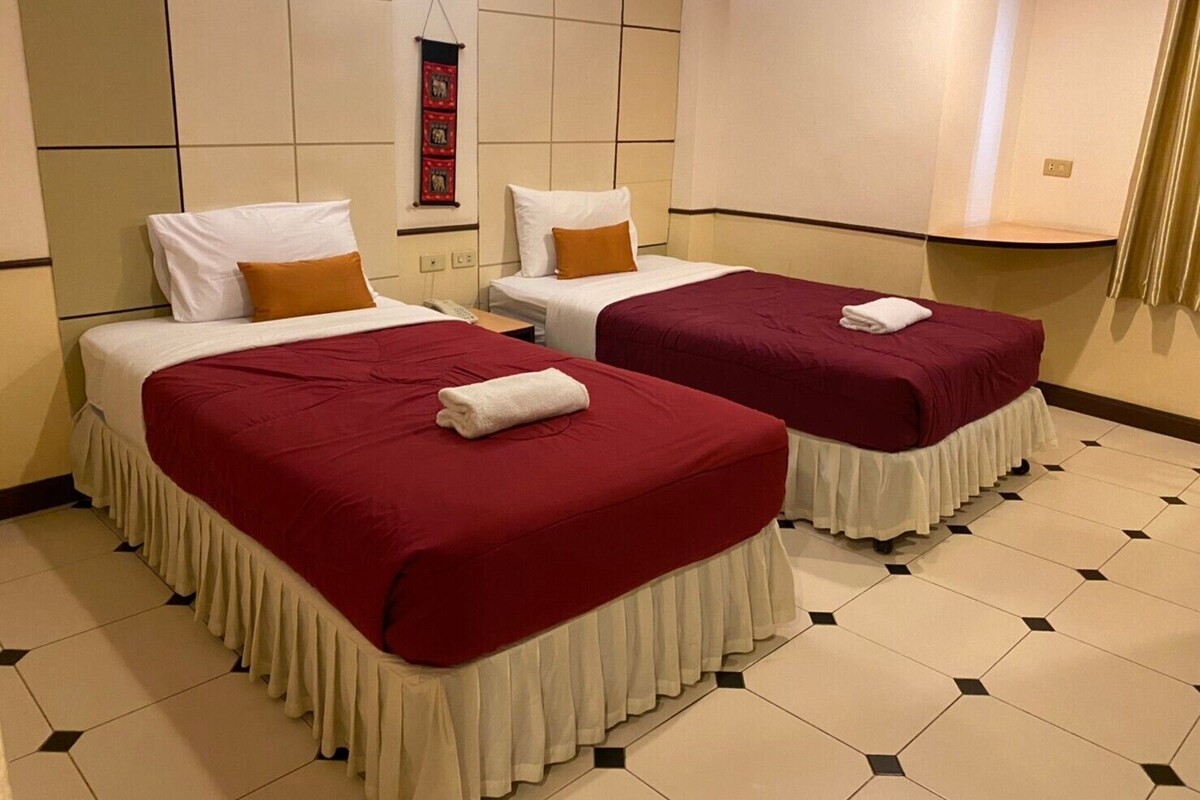 A hotel room with two beds, each with a red bedspread and white pillows, and a small table between them.