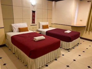 A hotel room with two beds, each with a red bedspread and white pillows, and a small table between them. - Honey House 2 (Bangkok)