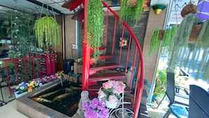 A spiral staircase with red railings, surrounded by hanging plants and a koi pond. - Honey House 2 (Bangkok)