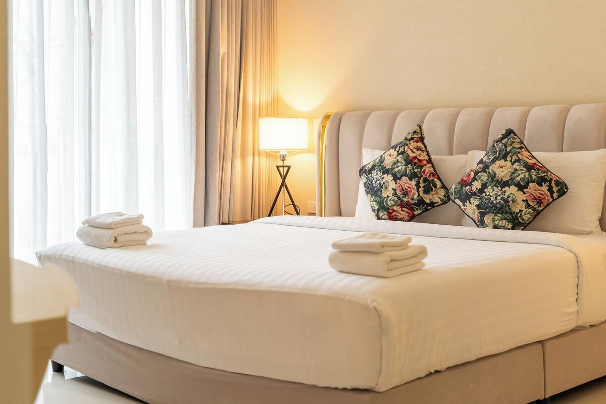 A neatly made bed with two pillows, a bedside lamp, and a window with curtains.