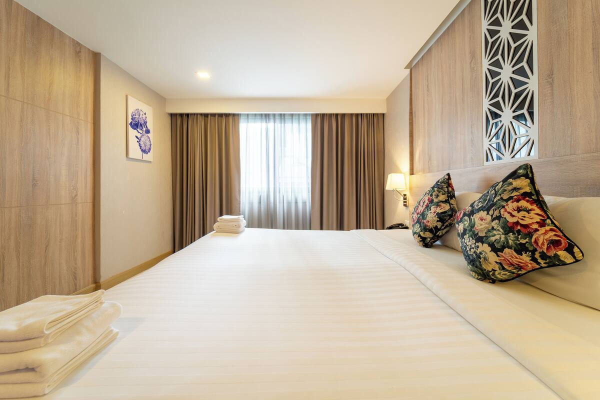 A hotel room with a large bed, a bedside table with a lamp, and a decorative wall panel.