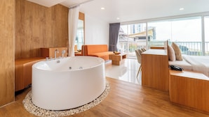 A modern bathroom with a large bathtub, wooden flooring, and a view of a cityscape through large windows. - Rodina Beach Hotel (Pattaya)