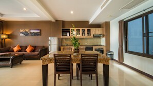 A modern living room with a sofa, coffee table, and dining area with chairs and a table. - Kamala Beachfront Apartment (Kamala)