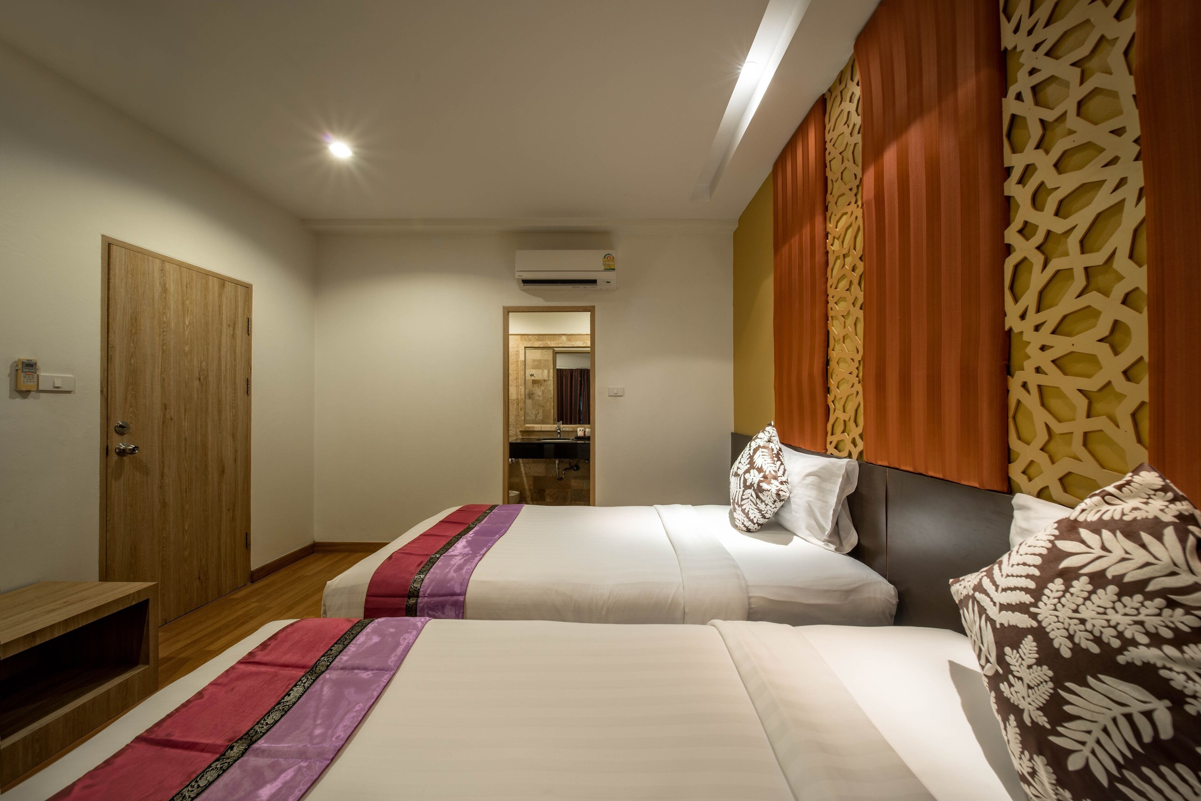 A hotel room with two beds, a wooden wardrobe, a small table, and a bathroom visible through an open door.