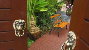 A wooden door with a lion head knocker, a bench, and a statue in a garden. - Kamala Beachfront Apartment (Kamala)