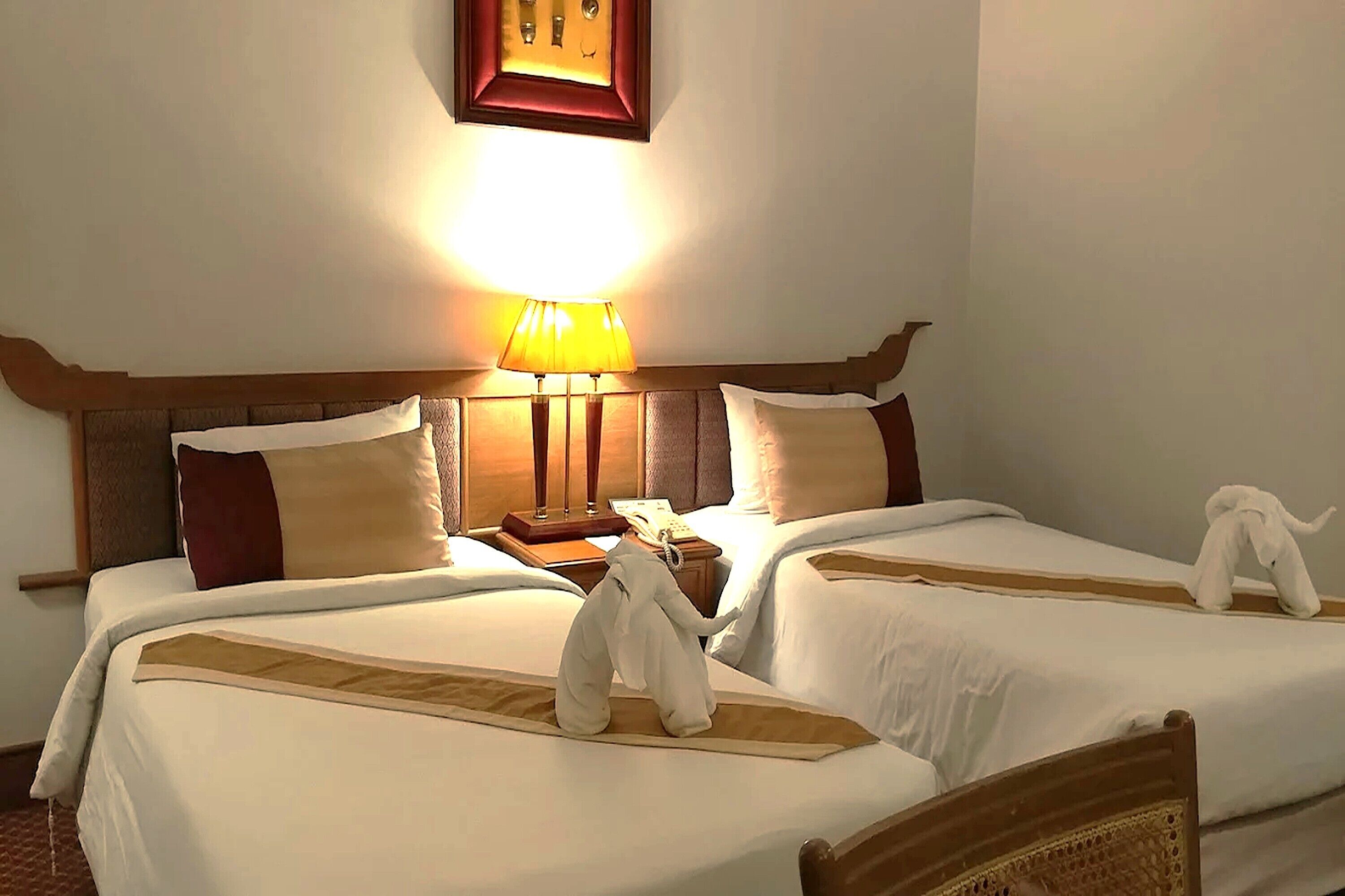 A hotel room with two beds, a bedside lamp, a telephone, and a framed picture on the wall.