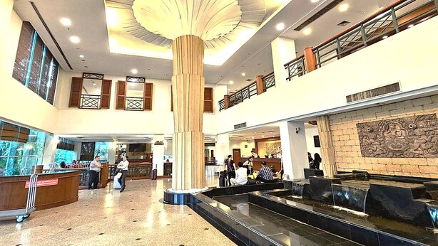 Um hall amplo com uma coluna central, um elemento de água e uma mesa de recepção.