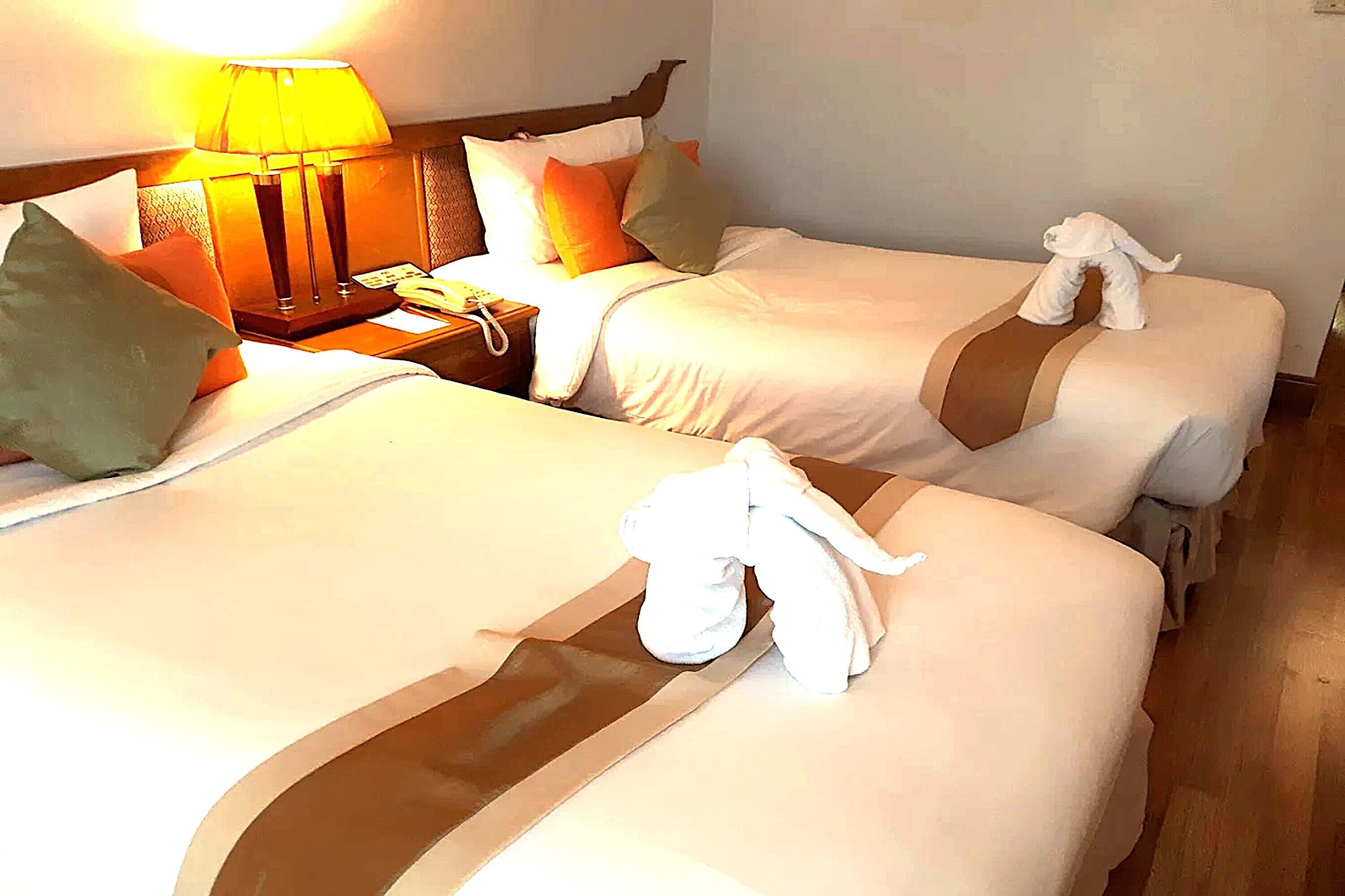 A hotel room with two beds, a nightstand with a lamp, and a towel rack with a towel and a plush toy.