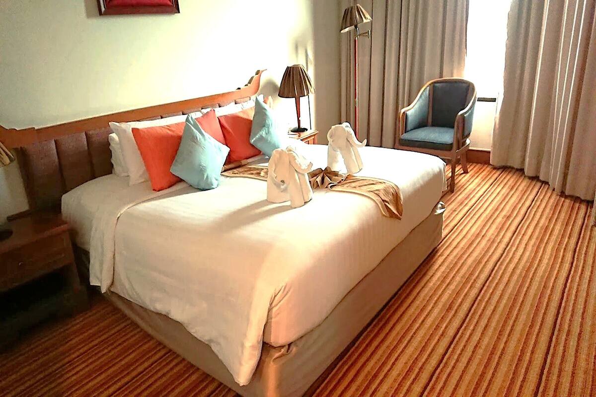 A hotel room with a large bed, a chair, a lamp, and a window with curtains.