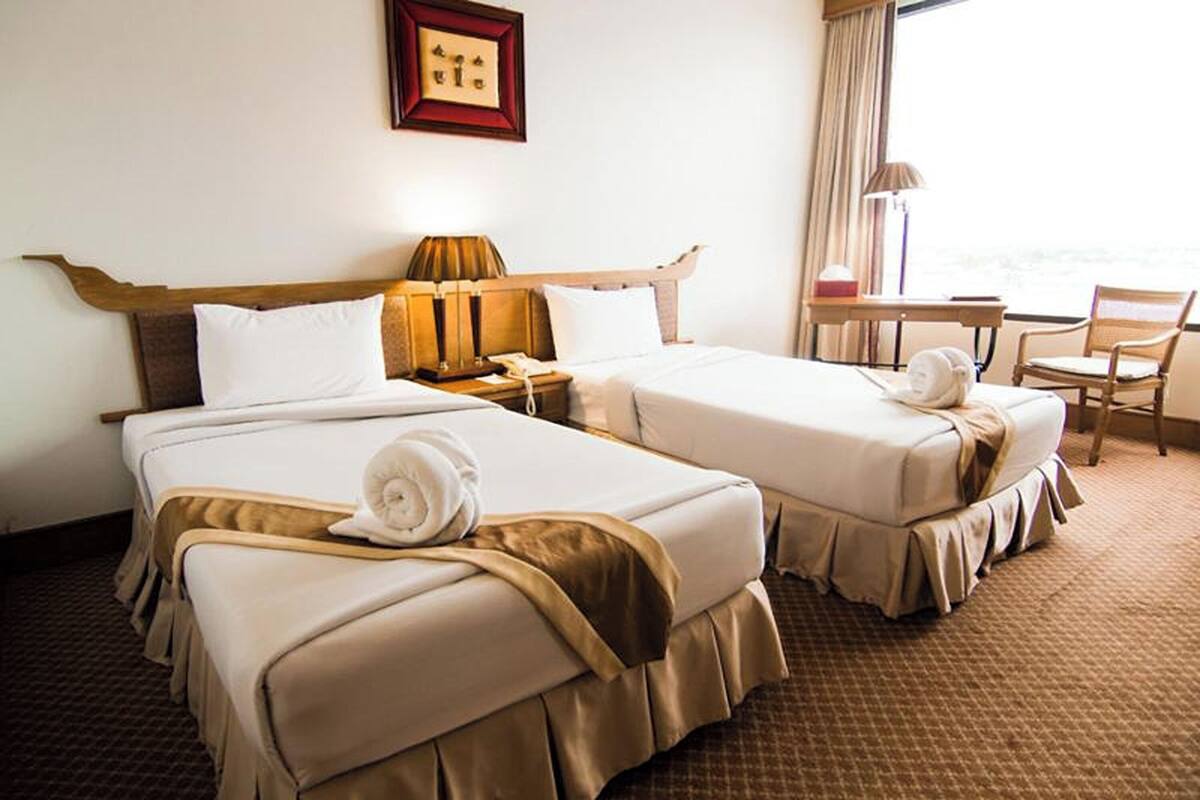 A hotel room with two beds, a desk, a chair, and a window with a view.