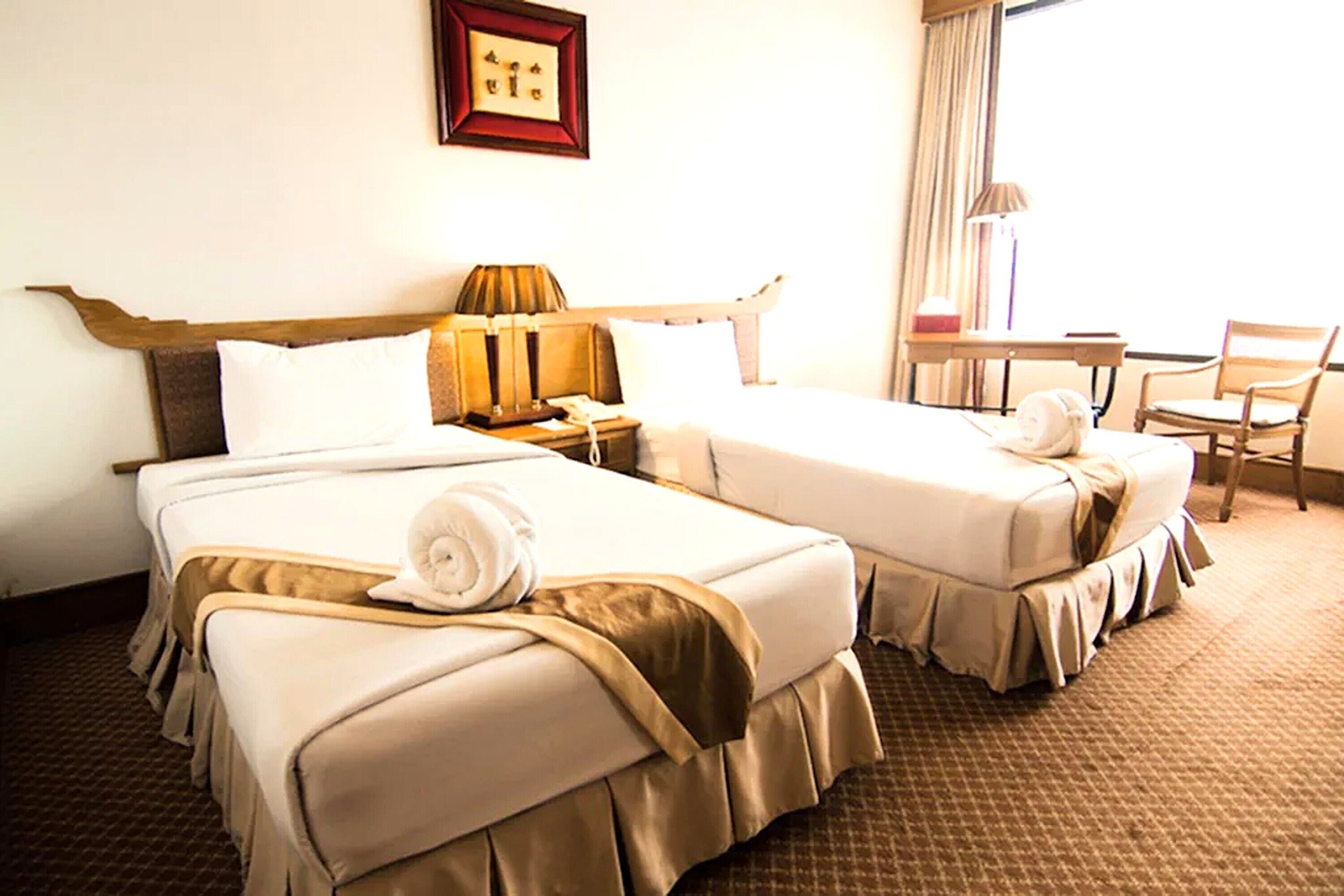 Ein Hotelzimmer mit zwei Betten, einem Schreibtisch, einem Stuhl und einem Fenster mit Vorhängen.