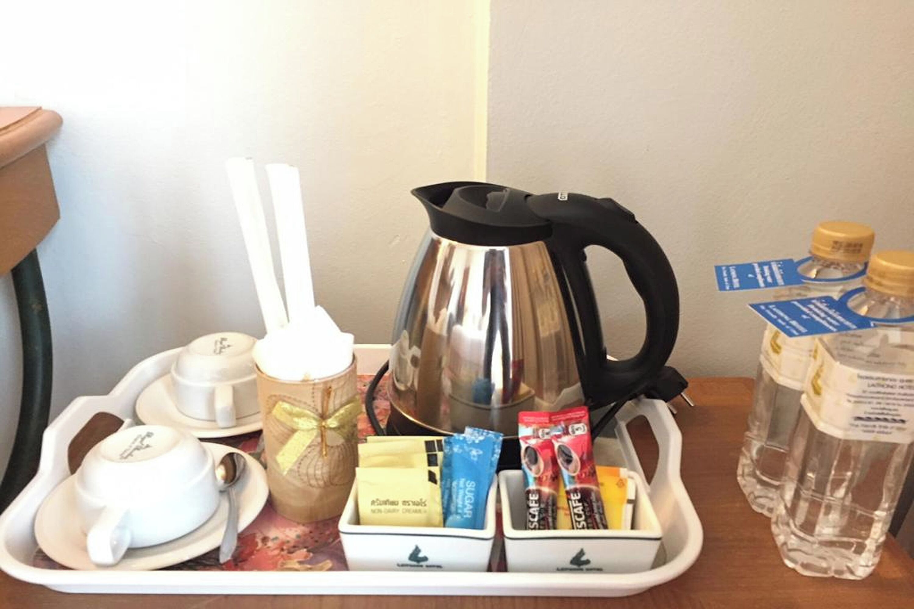 A tray with a coffee pot, tea cups, a jar, coffee packets, and water bottles.