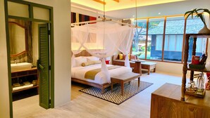 Un dormitorio con cama a dosel, una sala de estar con una mesa y sillas, y vistas al exterior a través de amplias ventanas.