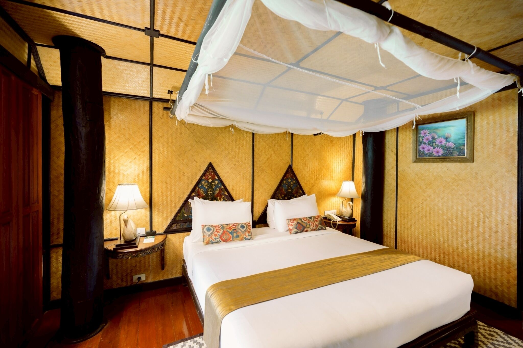 A hotel room with a bed, nightstands, a lamp, a canopy, and a painting on the wall.