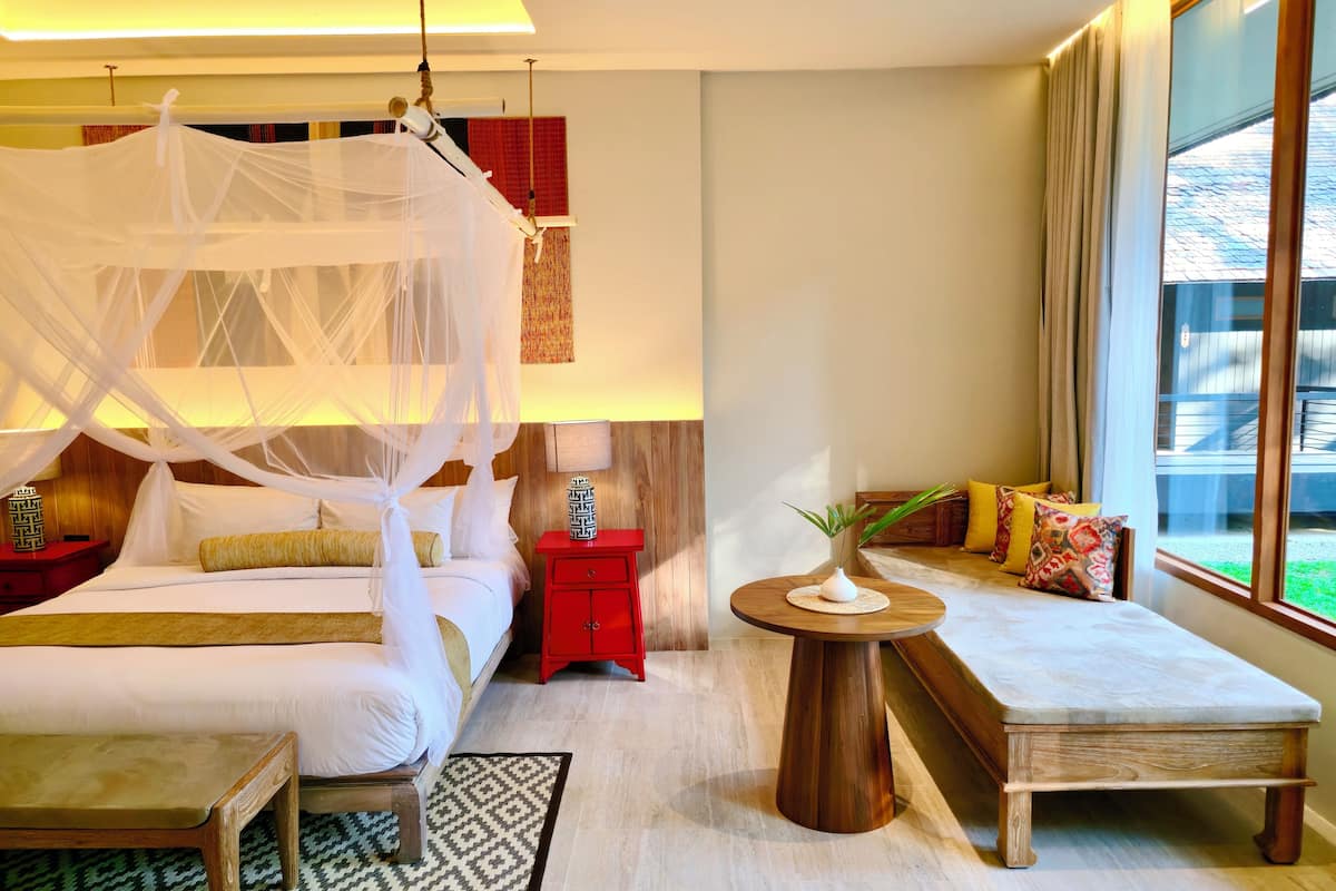 A bedroom with a four-poster bed, a bedside table with a lamp, a small wooden table, and a bench with cushions.