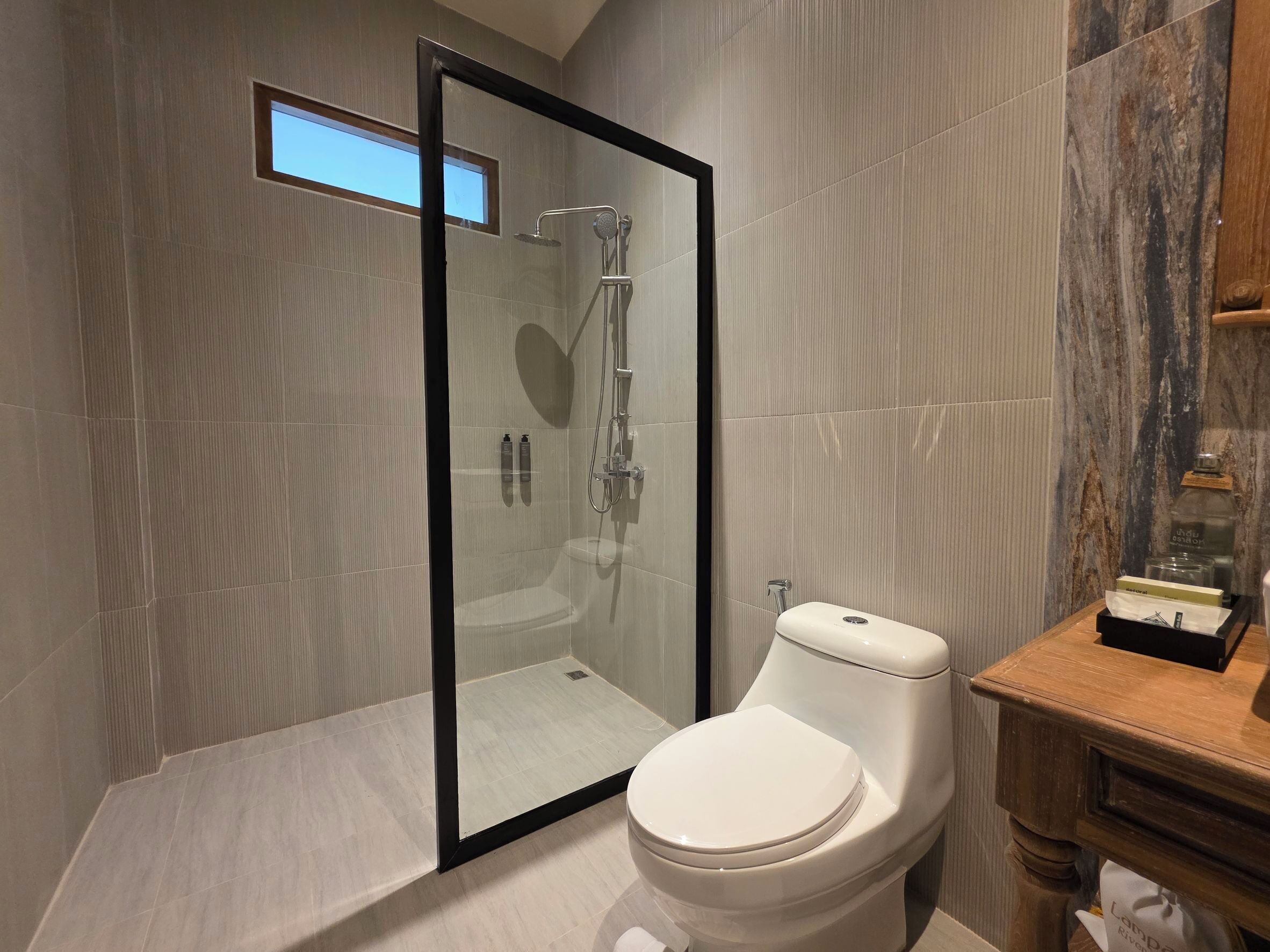 A modern bathroom with a glass-enclosed shower, a white toilet, and a wooden vanity.