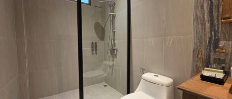 Un baño moderno con ducha envuelta en vidrio, inodoro blanco y tocador de madera.
