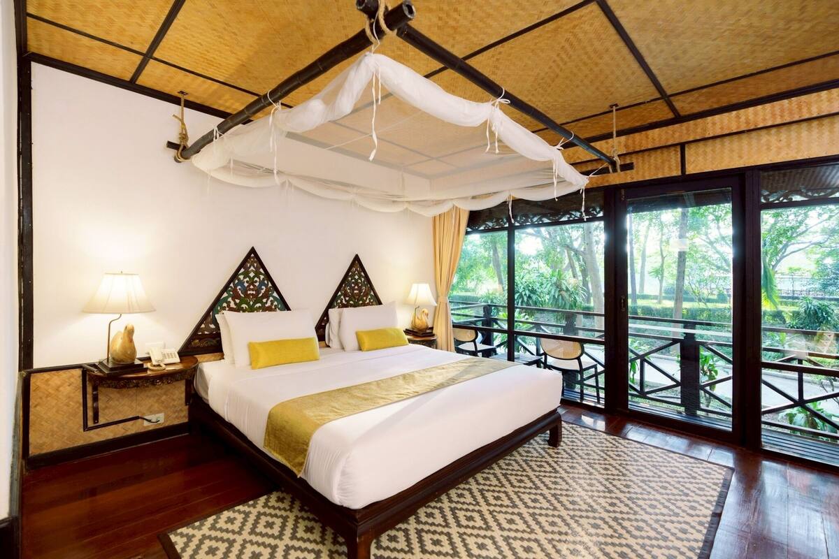 A spacious bedroom with a large bed, a canopy, and a view of the outdoors through large windows.