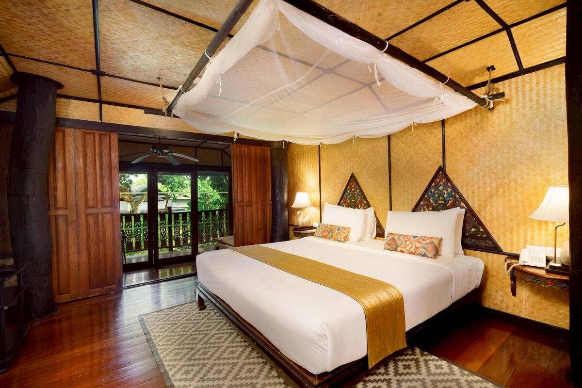 A spacious bedroom with a large bed, a canopy, and a view of greenery outside.