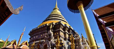 A traditional temple with a large golden spire, intricate carvings, and a prominent golden column.