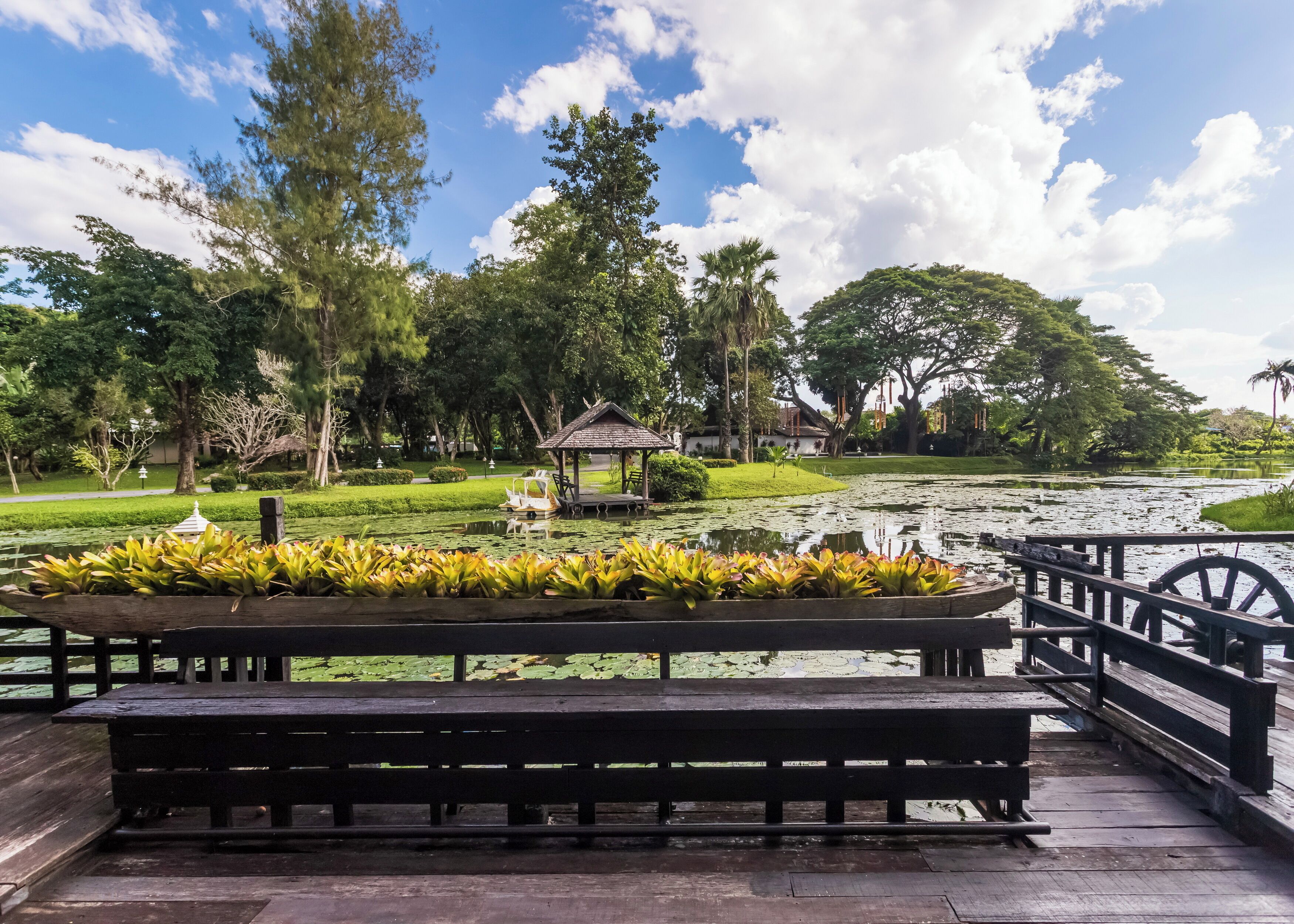 A wooden deck with benches overlooking a pond with a gazebo and a boat.