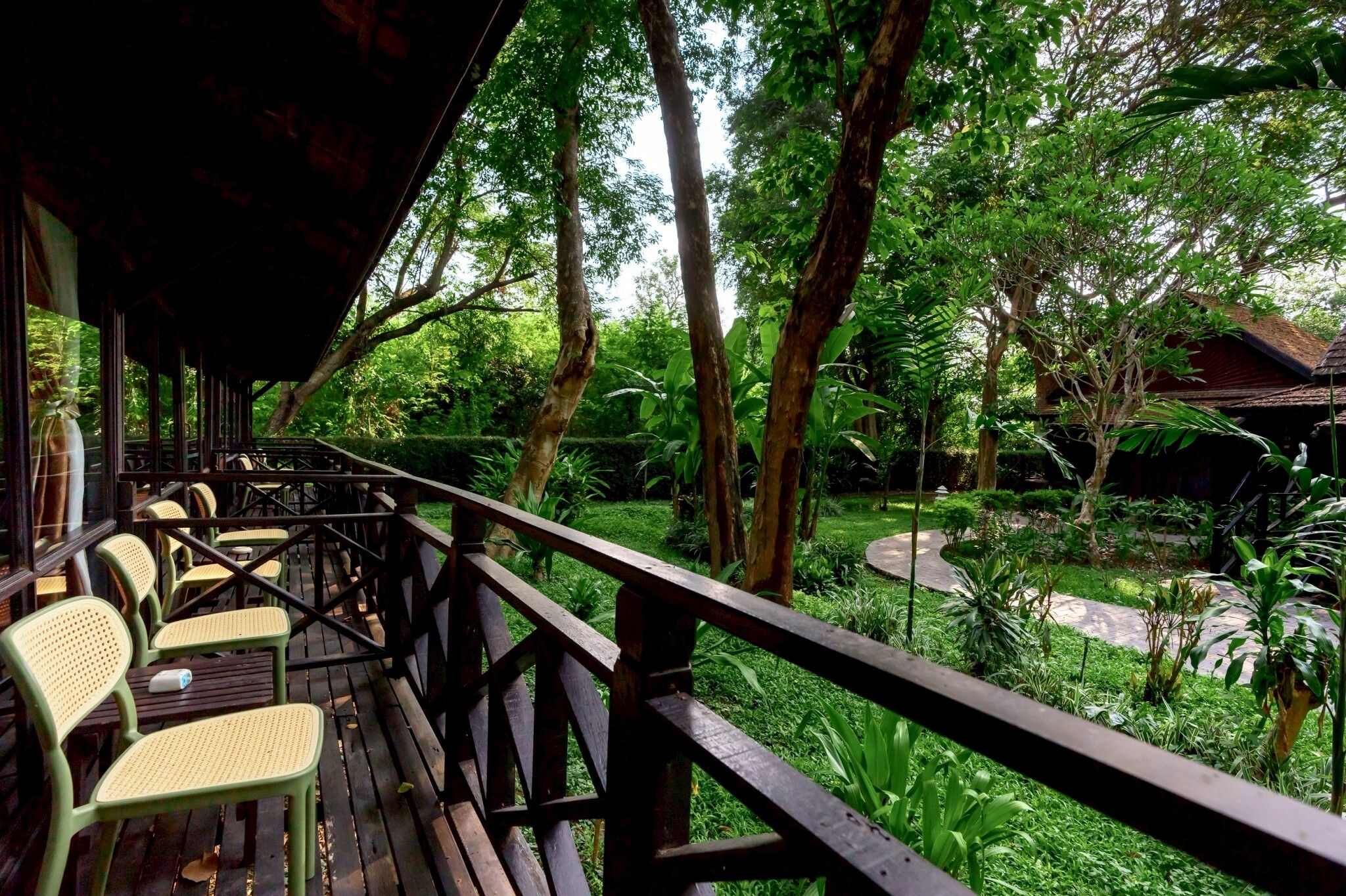 A wooden deck with chairs and tables, surrounded by lush greenery and trees.