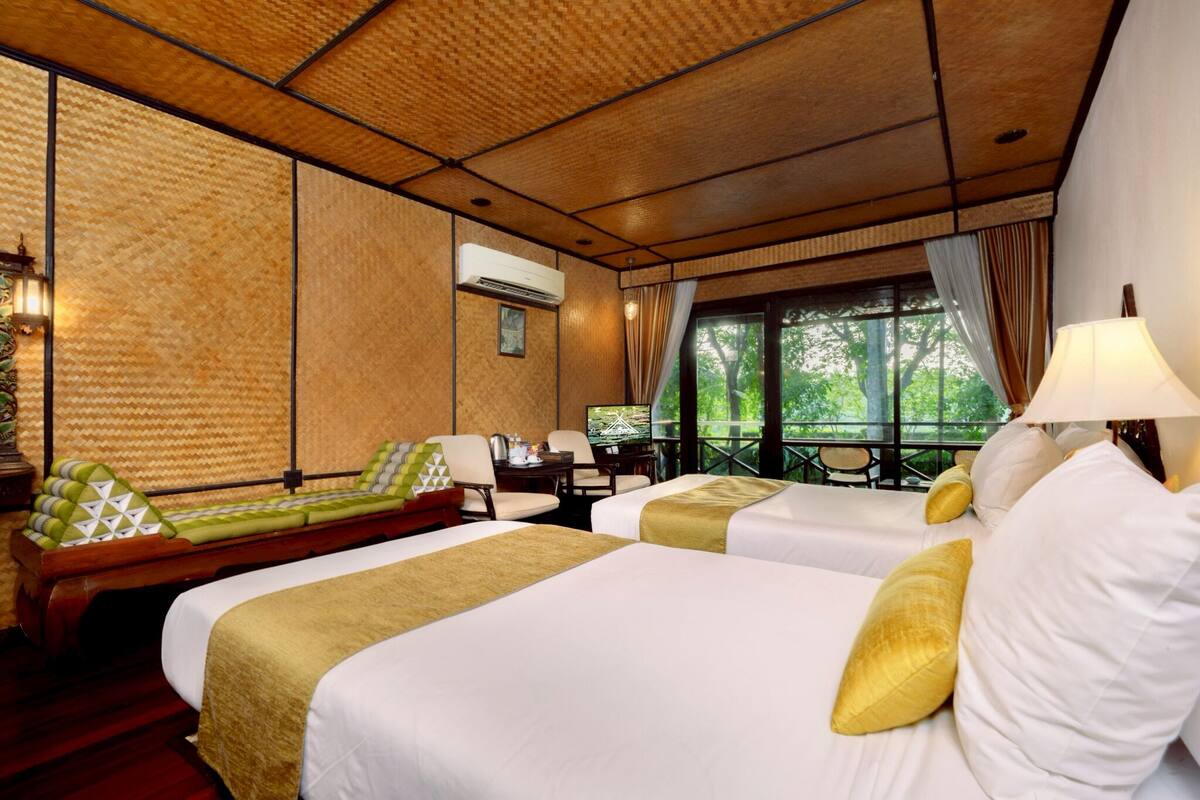 A hotel room with two beds, a desk, and a view of greenery.