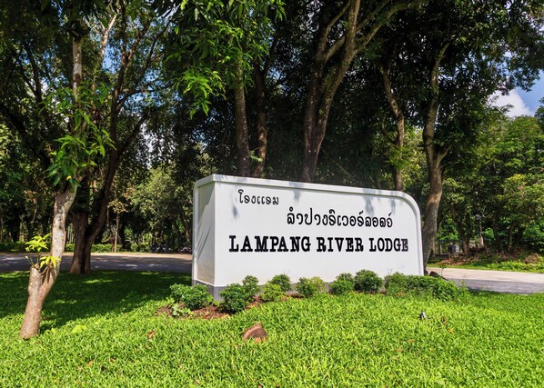 Señal de Lampang River Lodge, con un césped verde exuberante y árboles al fondo.