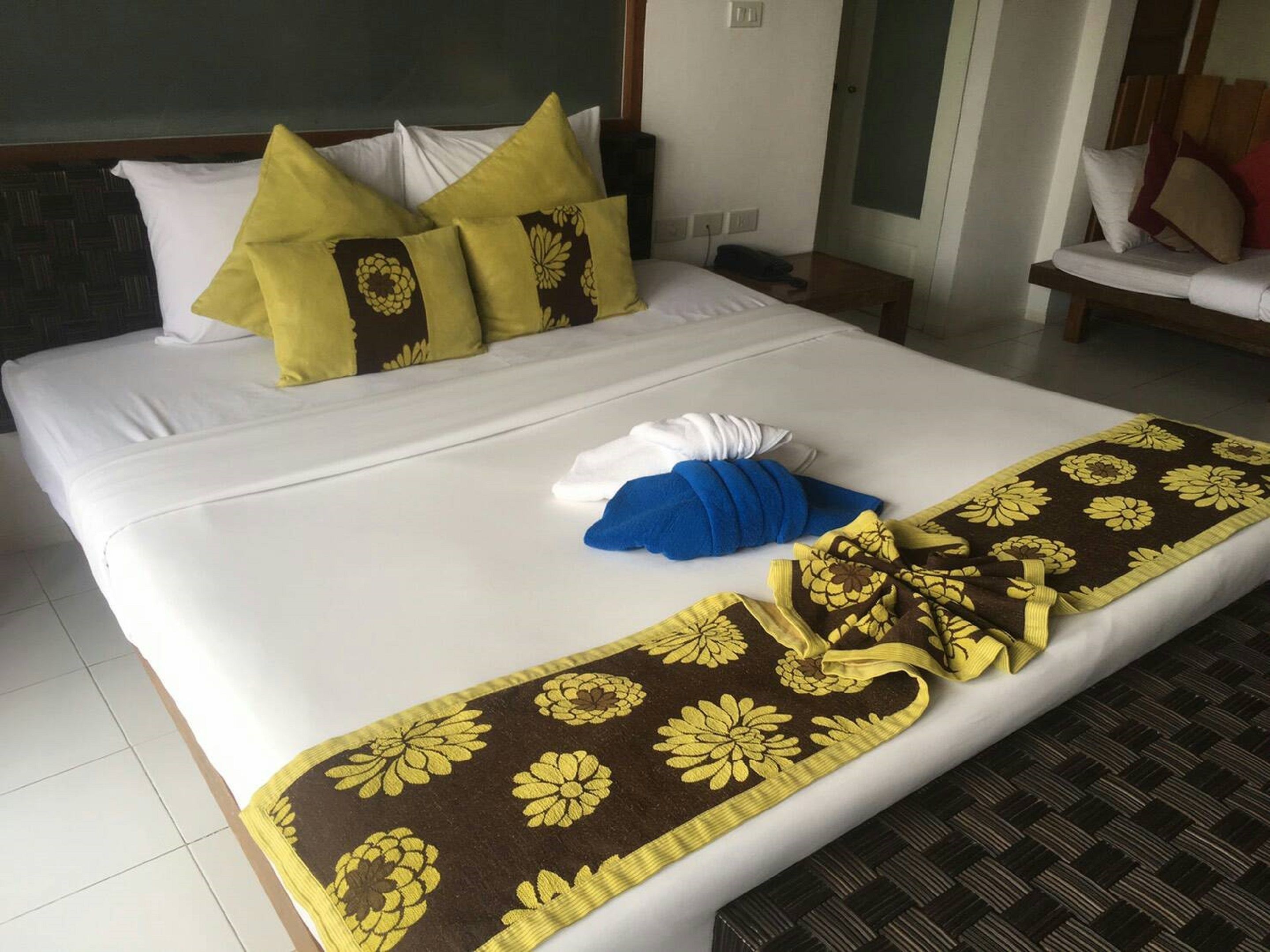 A neatly made bed with white linens, a brown and yellow floral bedspread, and a blue towel folded on the bed.