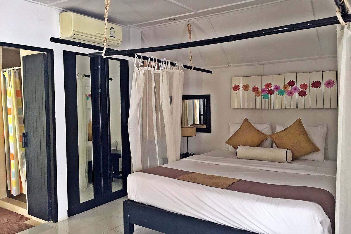 Quarto com cama, mesa de cabeceira, espelho e um ornamento floral na parede.