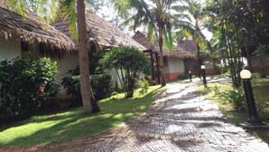 Un sendero bordeado por palmeras y edificios con techo de paja, evocando un entorno de resort tropical.