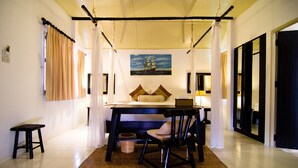Una habitación con una cama, una mesa y una silla. Hay un cuadro en la pared y una lámpara sobre la mesa.