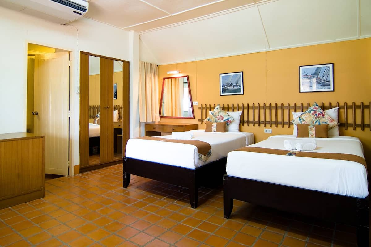 Quarto de hotel com duas camas, um guarda-roupa de madeira, um espelho e chão ladrilhado.