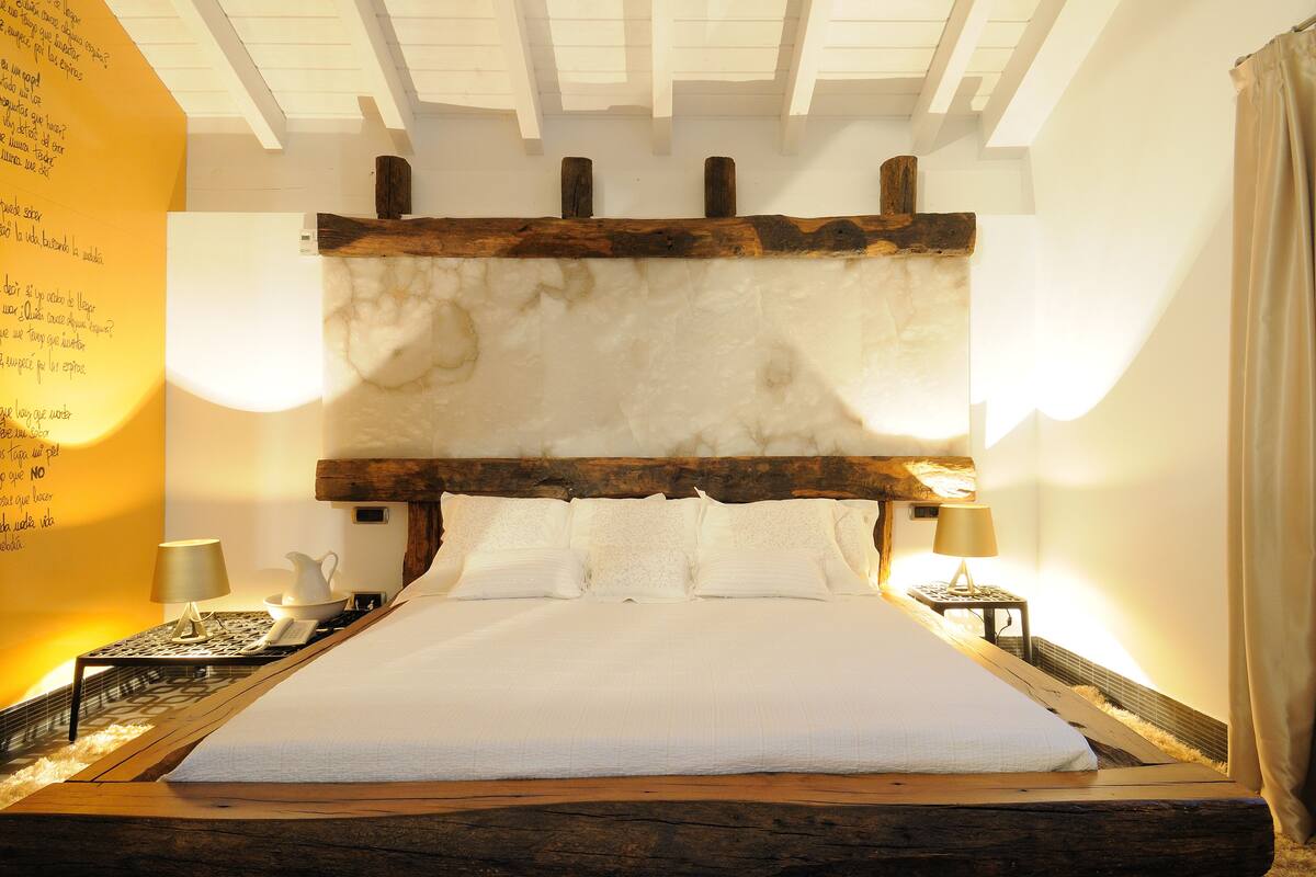 A large bed with a wooden headboard, two bedside tables with lamps, and a wall with text.