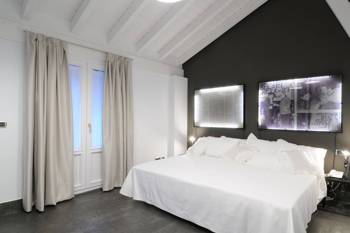 A modern bedroom with a large bed, a dark accent wall, and two illuminated wall art pieces.