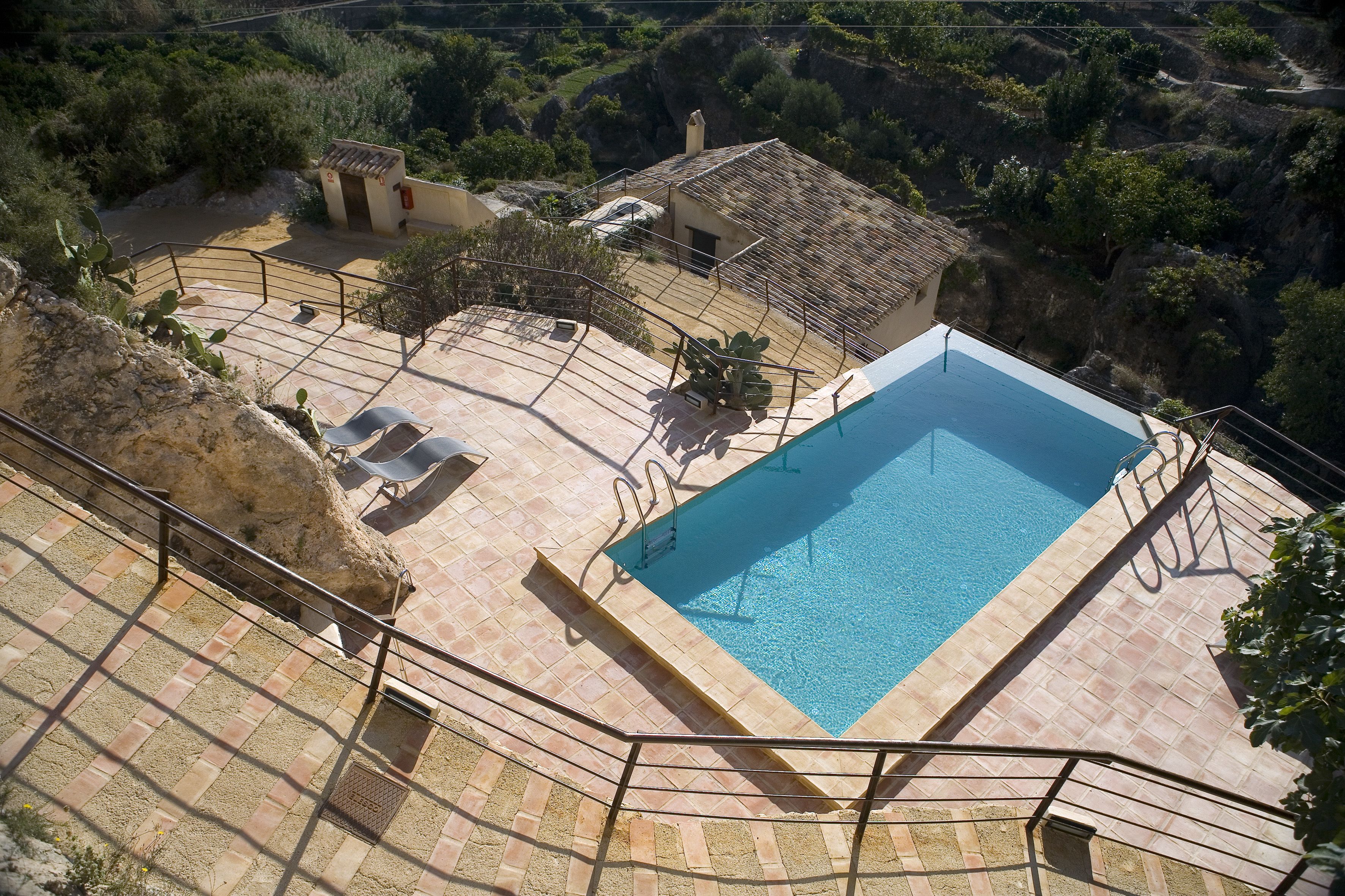 A swimming pool with a tiled deck, a small building, and a stone wall.