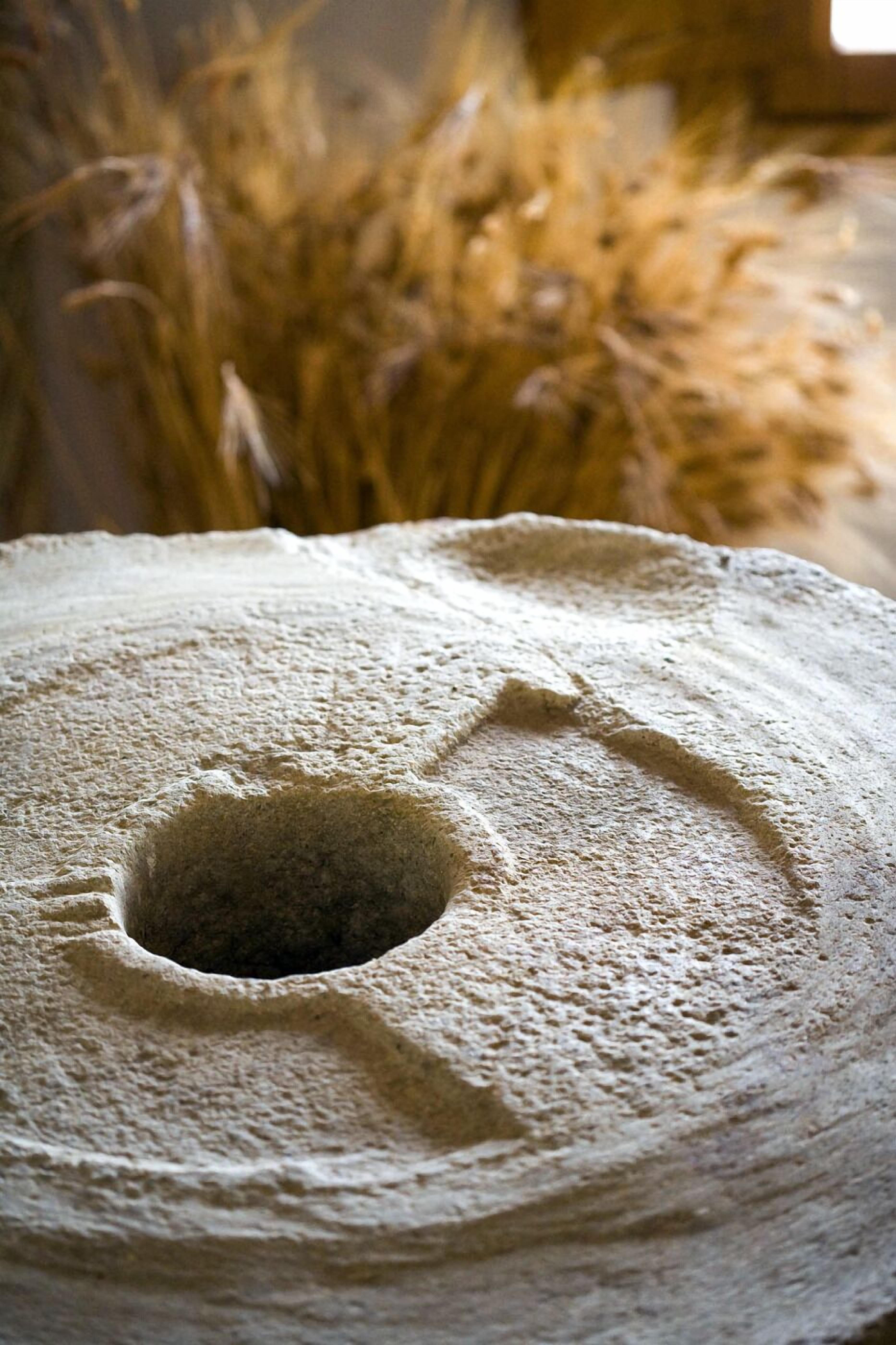 Un moulin en pierre doté d’un trou central, entouré de tiges de blé.