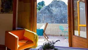 A room with a wooden ceiling, a bed with white linens, an orange chair, and a view of a mountain through an open door. -  Hospedería Bajo el Cejo  (Alhama de Murcia)