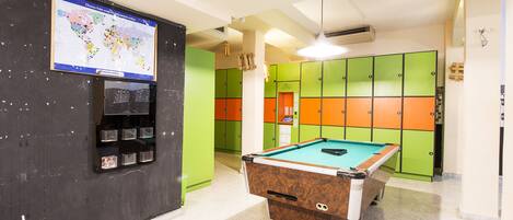 Une table de billard dans une pièce où se trouvent des casiers colorés et une carte accrochée au mur.