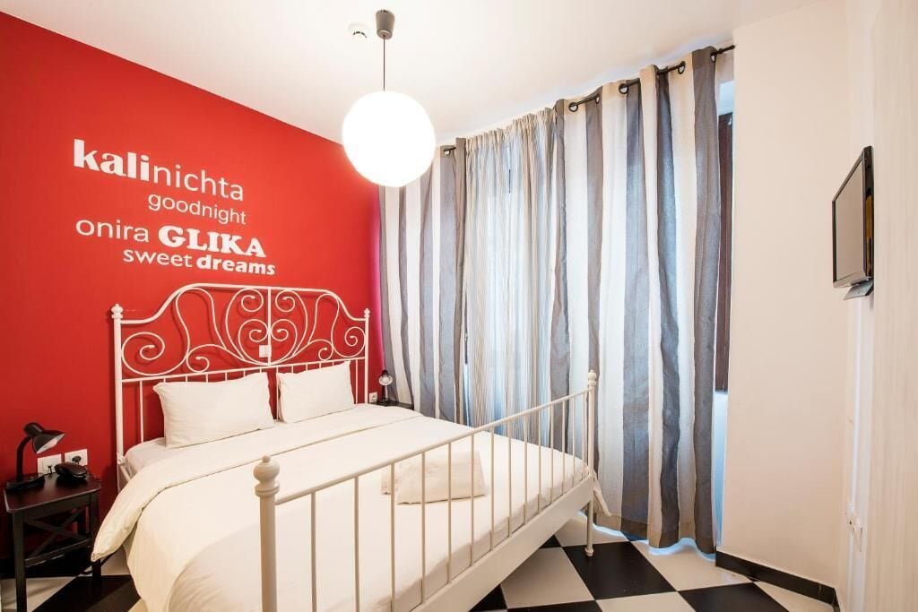 A bedroom with a white metal bed frame, a red accent wall, and a black and white checkered floor.