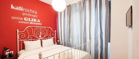 A bedroom with a white metal bed frame, a red accent wall, and a black and white checkered floor.