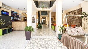 A spacious lobby with a reception desk, seating area, and a balcony with plants. - Safestay Athens Monastiraki (Athens)
