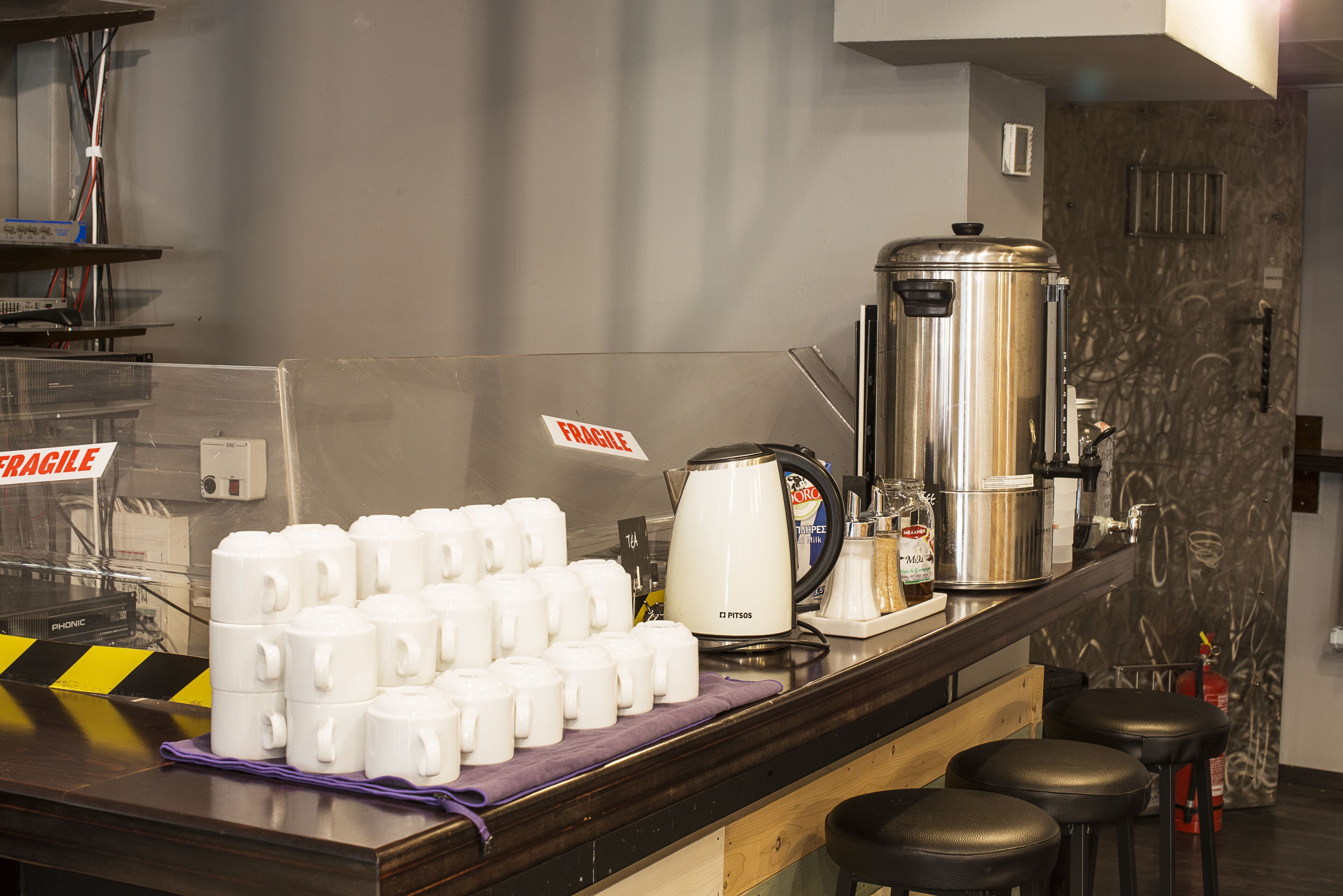 A kitchen counter with a coffee machine, a kettle, and a stack of white mugs.