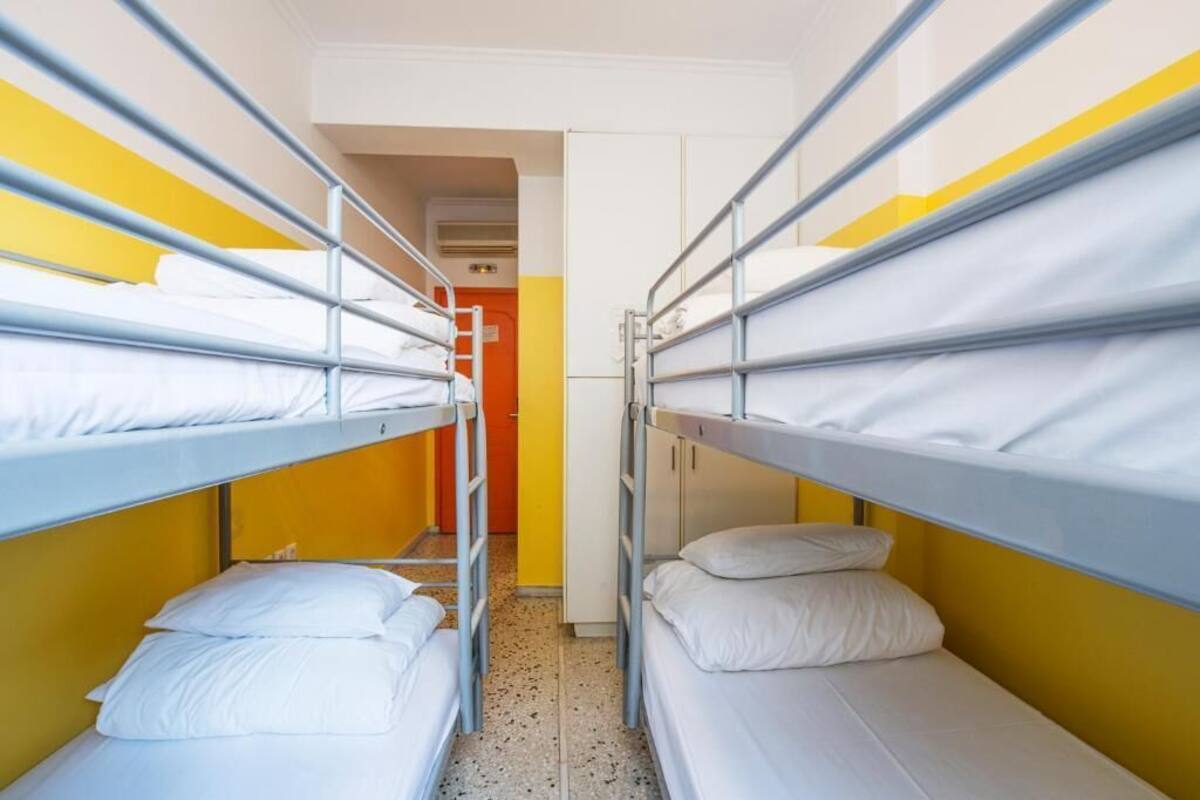 Un corredor estrecho con literas a ambos lados, una puerta al final y suelo de baldosas.